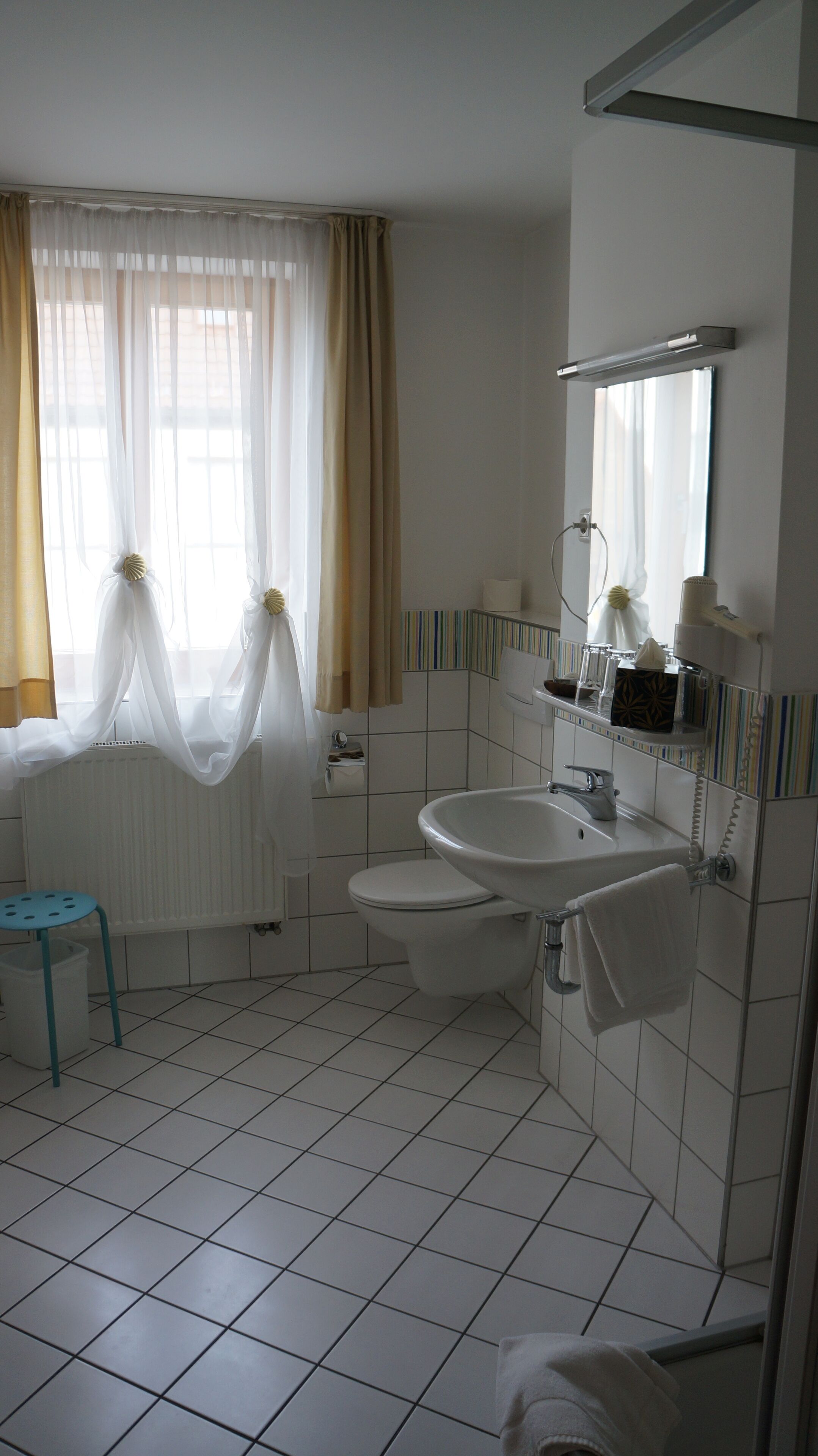 A bathroom with a white sink, toilet, and bathtub. There is a window with sheer curtains and a towel rack above the sink.