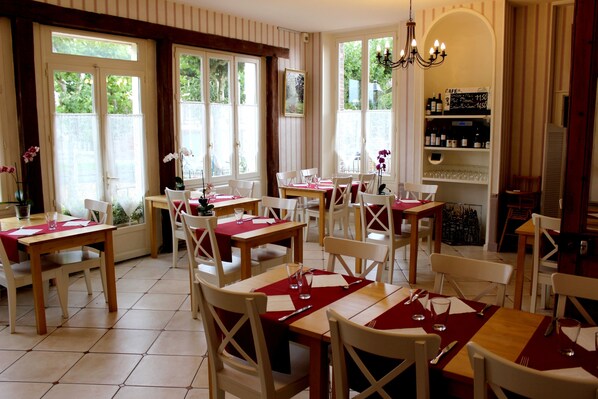 A dining area with tables set for four, white chairs, and a red tablecloth. - Hôtel les Aubépines (Illiers-Combray)