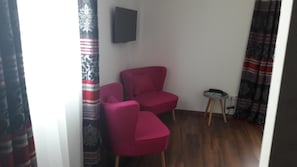 Una habitación con dos sillas rojas, una mesita con un teléfono y un televisor en la pared.