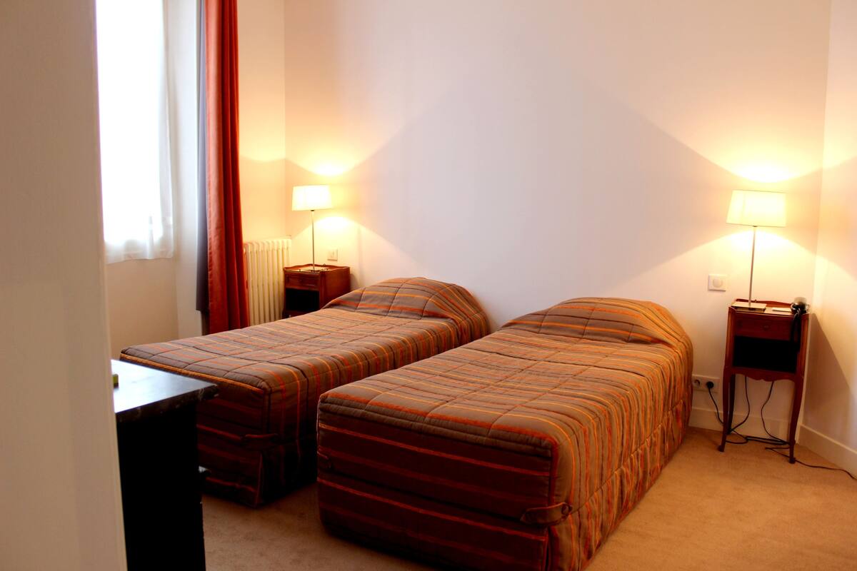 A hotel room with two single beds, a small table, and two bedside lamps.