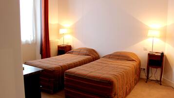 Habitación de hotel con dos camas individuales, una mesita y dos lámparas de noche.