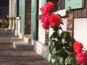 A row of red roses in front of a building with green shutters and a brick facade. - Hôtel les Aubépines (Illiers-Combray)