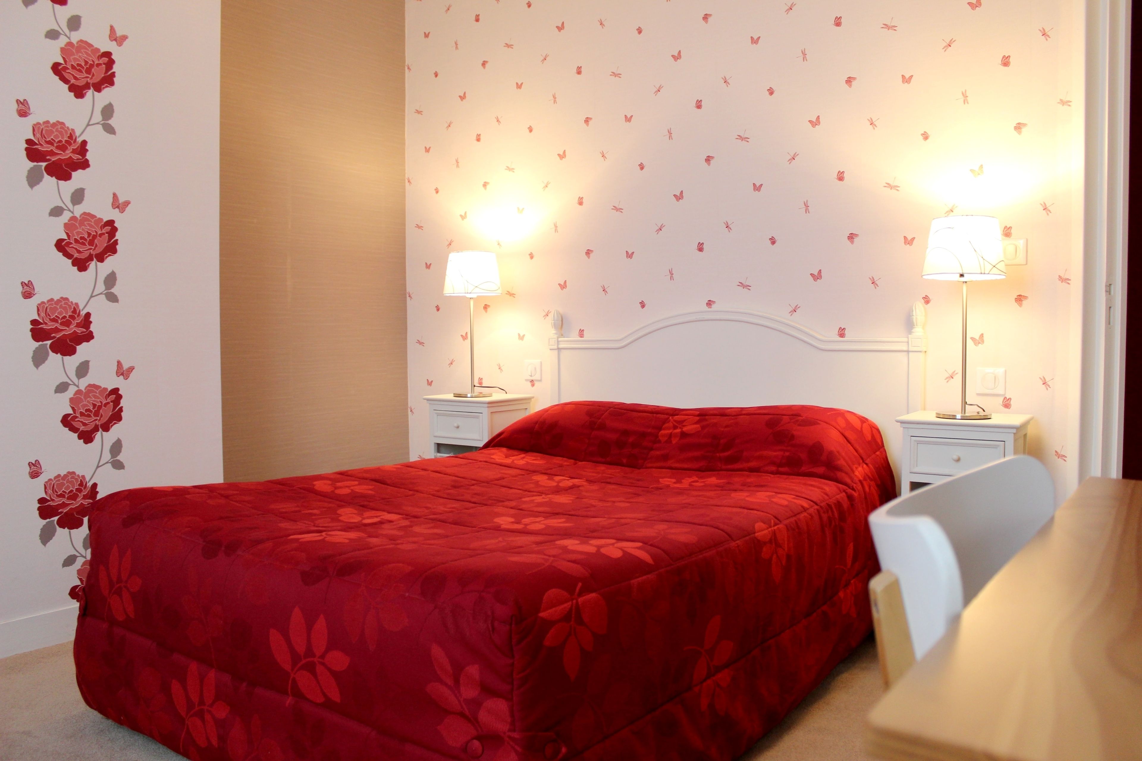 A bedroom with a red bedspread, two bedside lamps, a white nightstand, and a wall with butterfly decals.