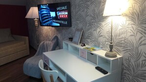 Habitación de hotel con un escritorio blanco, un televisor en la pared, una lámpara y un papel tapiz estampado.