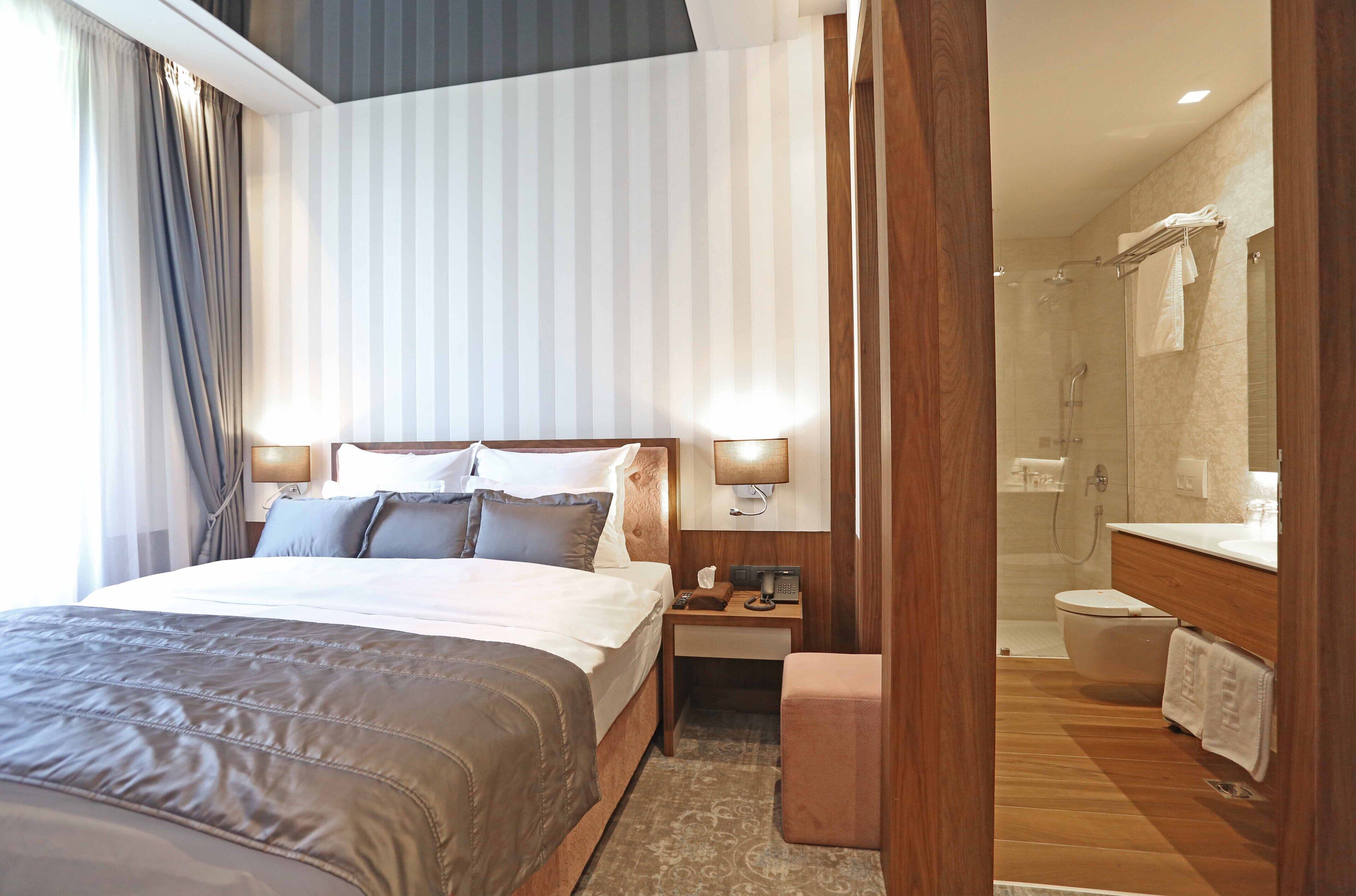A hotel room with a large bed, bedside tables, a nightstand, a bathroom with a shower, toilet, and sink.
