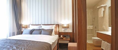 A hotel room with a large bed, bedside tables, a nightstand, a bathroom with a shower, toilet, and sink.