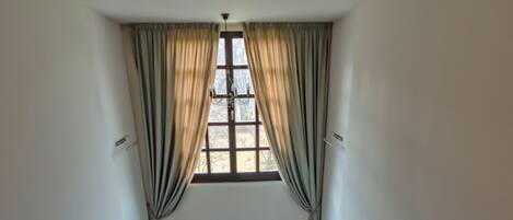 A staircase with a wooden handrail and metal balusters, leading to a landing with a window and curtains.