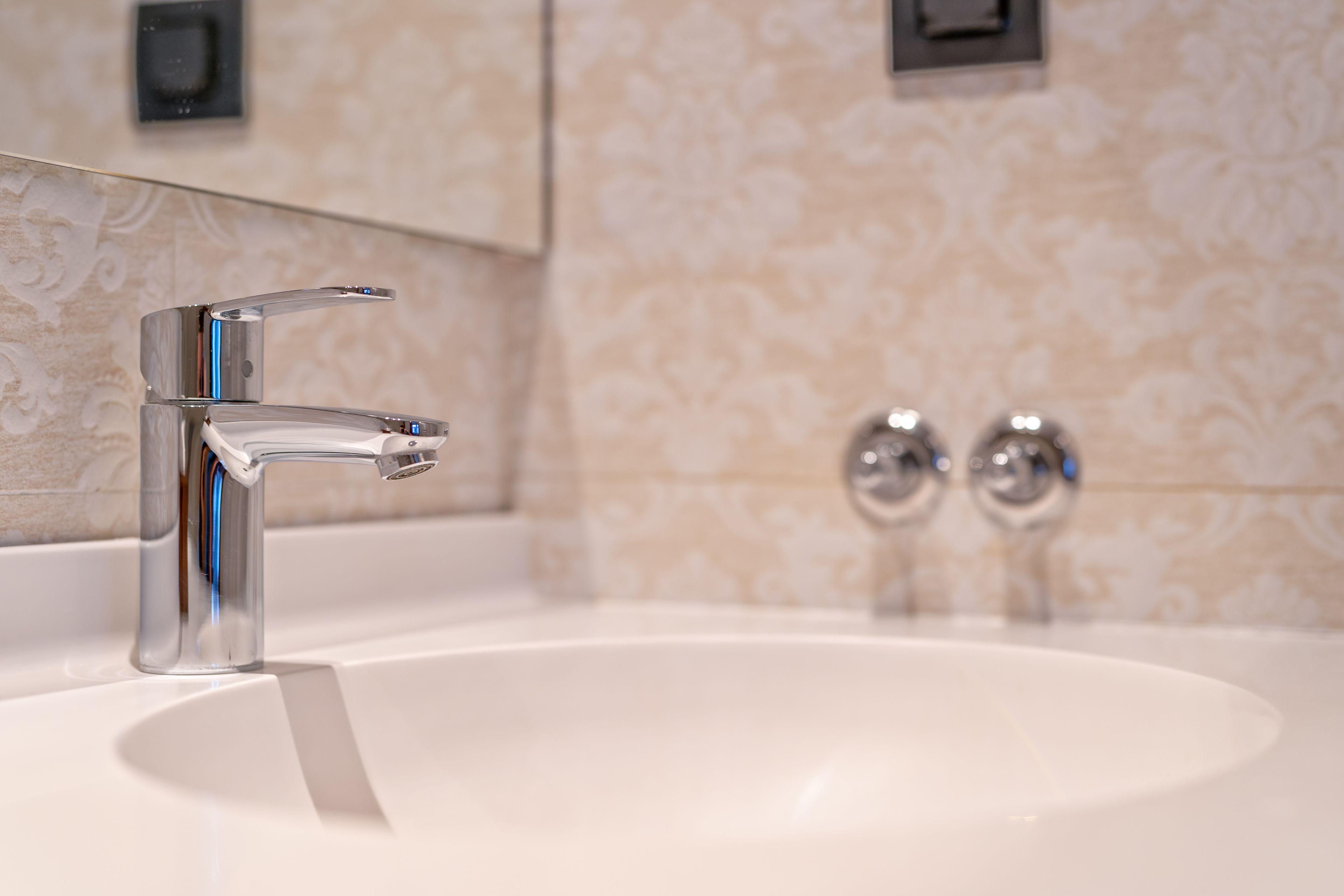 Un baño moderno con un grifo cromado, un lavamanos blanco y un papel tapiz con diseño.