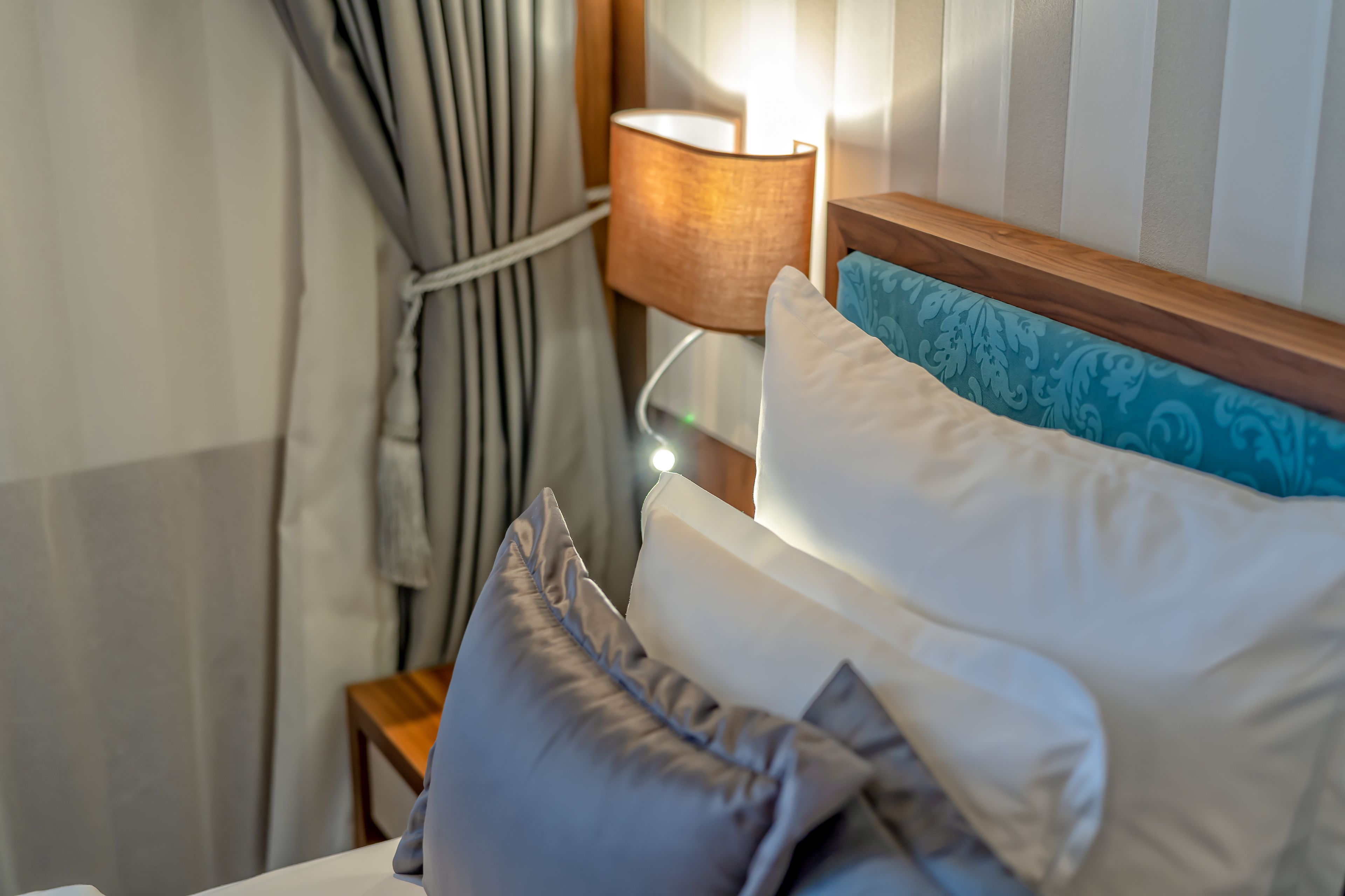 A neatly made bed with white and blue pillows, a wooden headboard, and a bedside lamp.