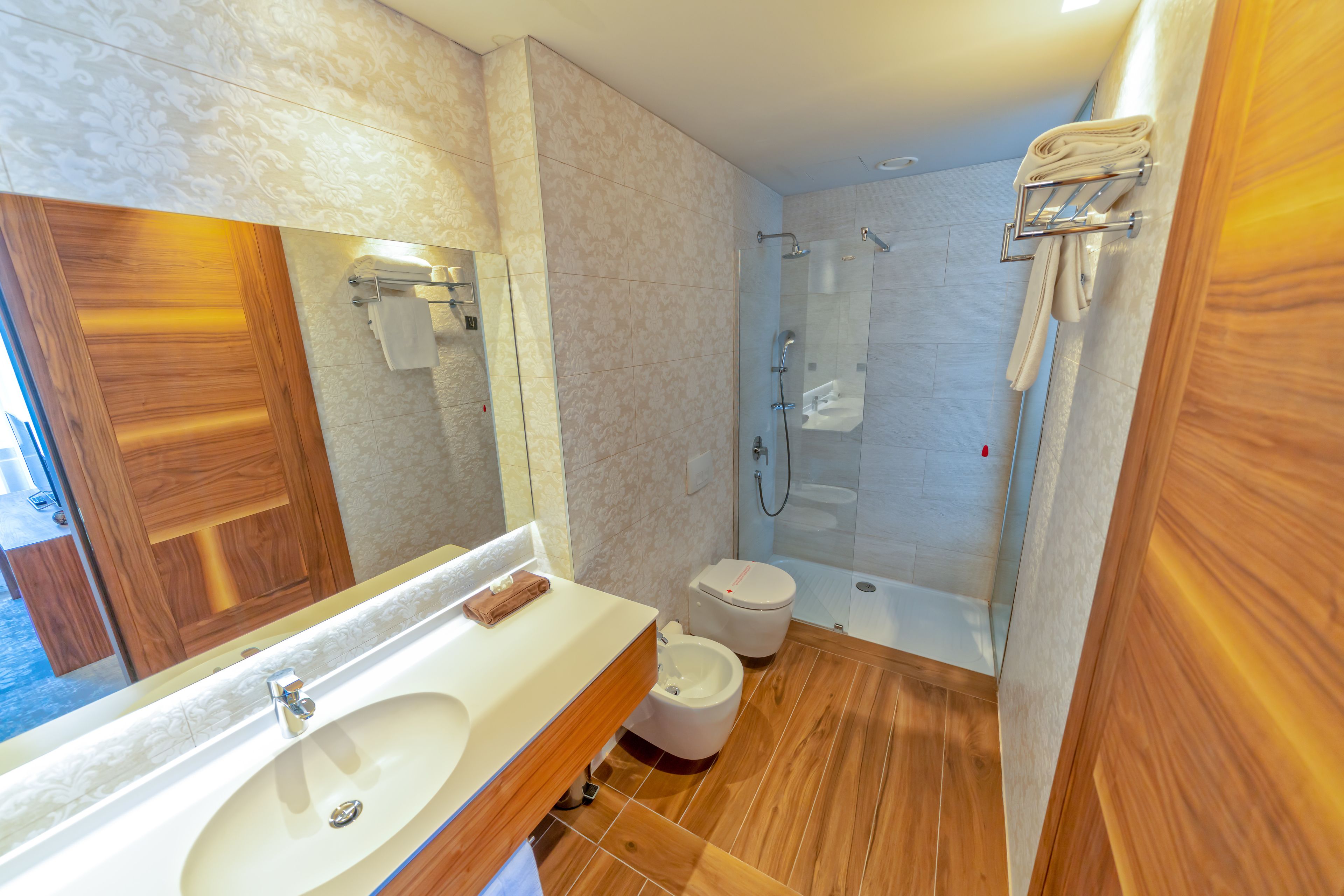 Un baño moderno con un espejo grande, un lavamanos, un inodoro y una zona de ducha.