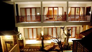 A two-story hotel with balconies, a swimming pool, and a well-lit interior. - Amed Sunset Beach (Karangasem)