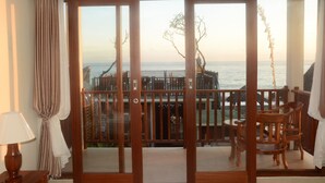 A room with a large sliding glass door leading to a balcony with a view of the sea. - Amed Sunset Beach (Karangasem)