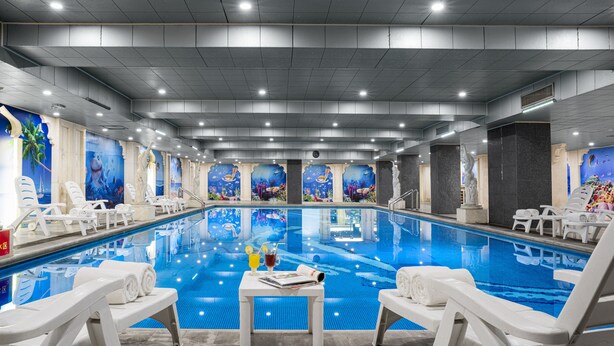 A large indoor swimming pool with white lounge chairs and tables, surrounded by murals of ocean scenes. - Country Garden Phoenix Hotel Chongqing (Chongqing)