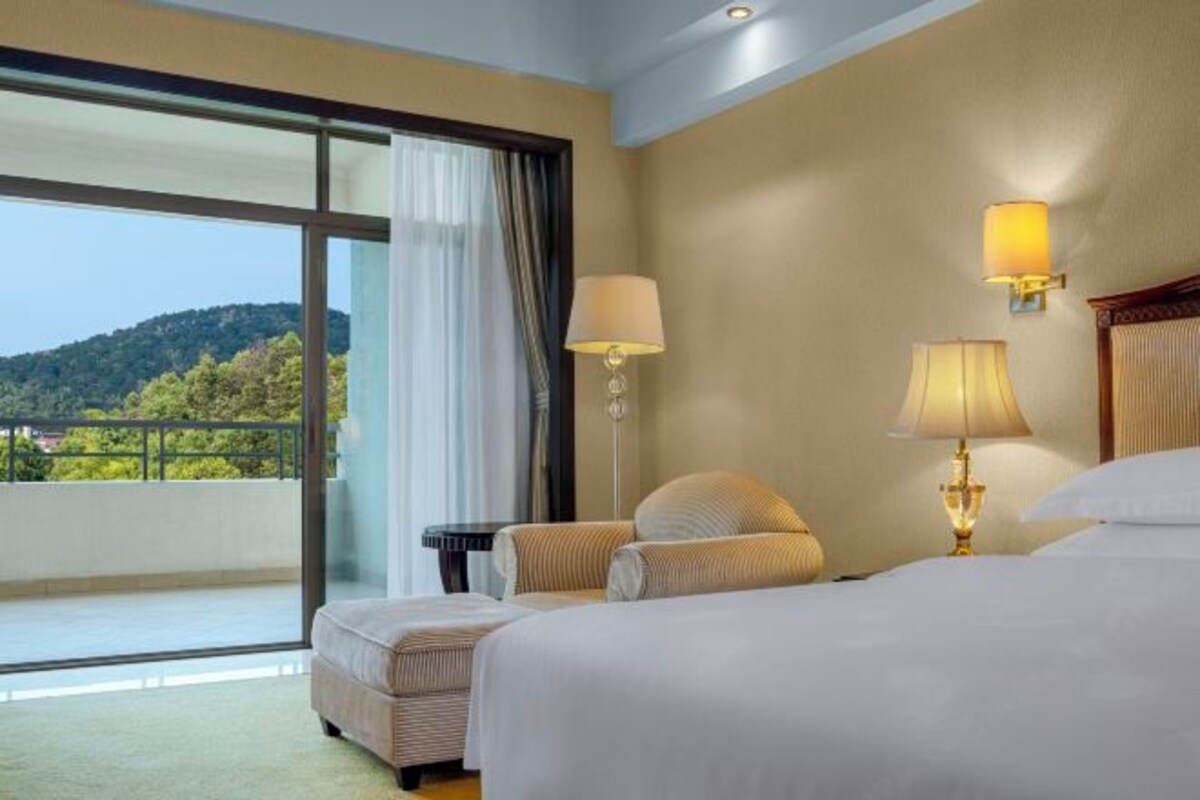 A hotel room with a large window, a bed, two bedside tables, and a lamp.