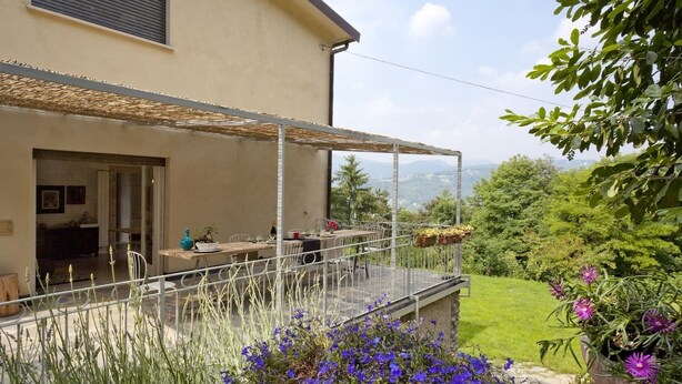Una casa amb un porxo cobert, un jardí ple de flors i vista als turons.