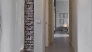 Un passadís estret amb una paret de maó d'un costat i un marc de porta de fusta de l'altre. Es pot veure, a la distància, una taula petita amb una làmpada i llibres.
