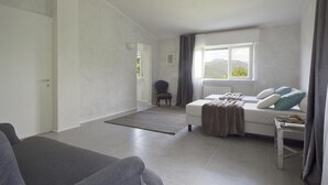 Habitació moderna i minimalista amb un llit, un sofà gris i una cadira.