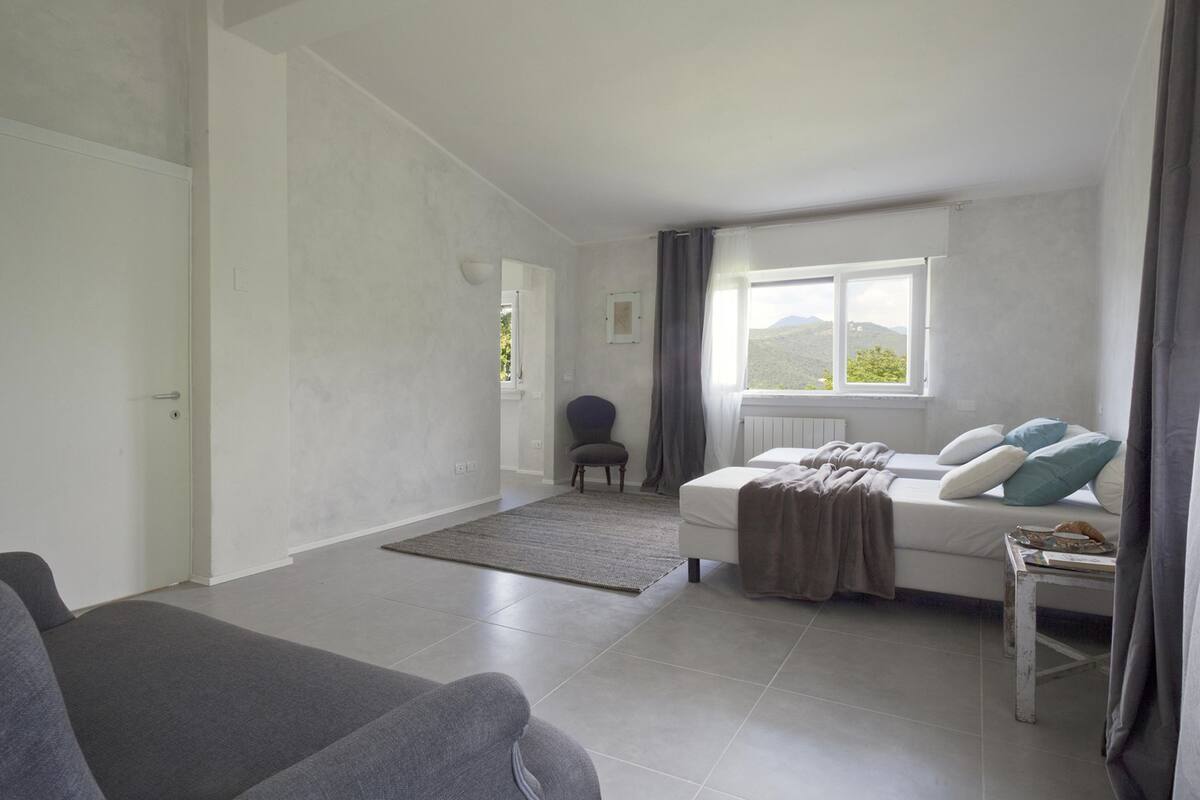 Ein modernes, minimalistisches Zimmer mit einem Bett, einem grauen Sofa und einem Sessel.