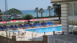 A pool area with blue lounge chairs and red umbrellas, a stone wall with a 'BOLD TASTE' sign, and a view of the ocean. - Olbia Residence Hotel (Konyaalti)