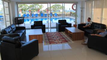 Vestíbulo de hotel con vista a la piscina, sofás de cuero, televisor y una planta en maceta.