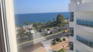 A modern building with a view of the sea and a busy street with cars and palm trees. - Olbia Residence Hotel (Konyaalti)