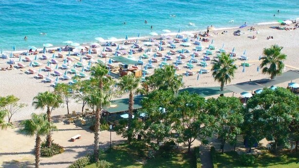 A beach with numerous umbrellas and lounge chairs, palm trees, and a clear view of the ocean. - Olbia Residence Hotel (Konyaalti)