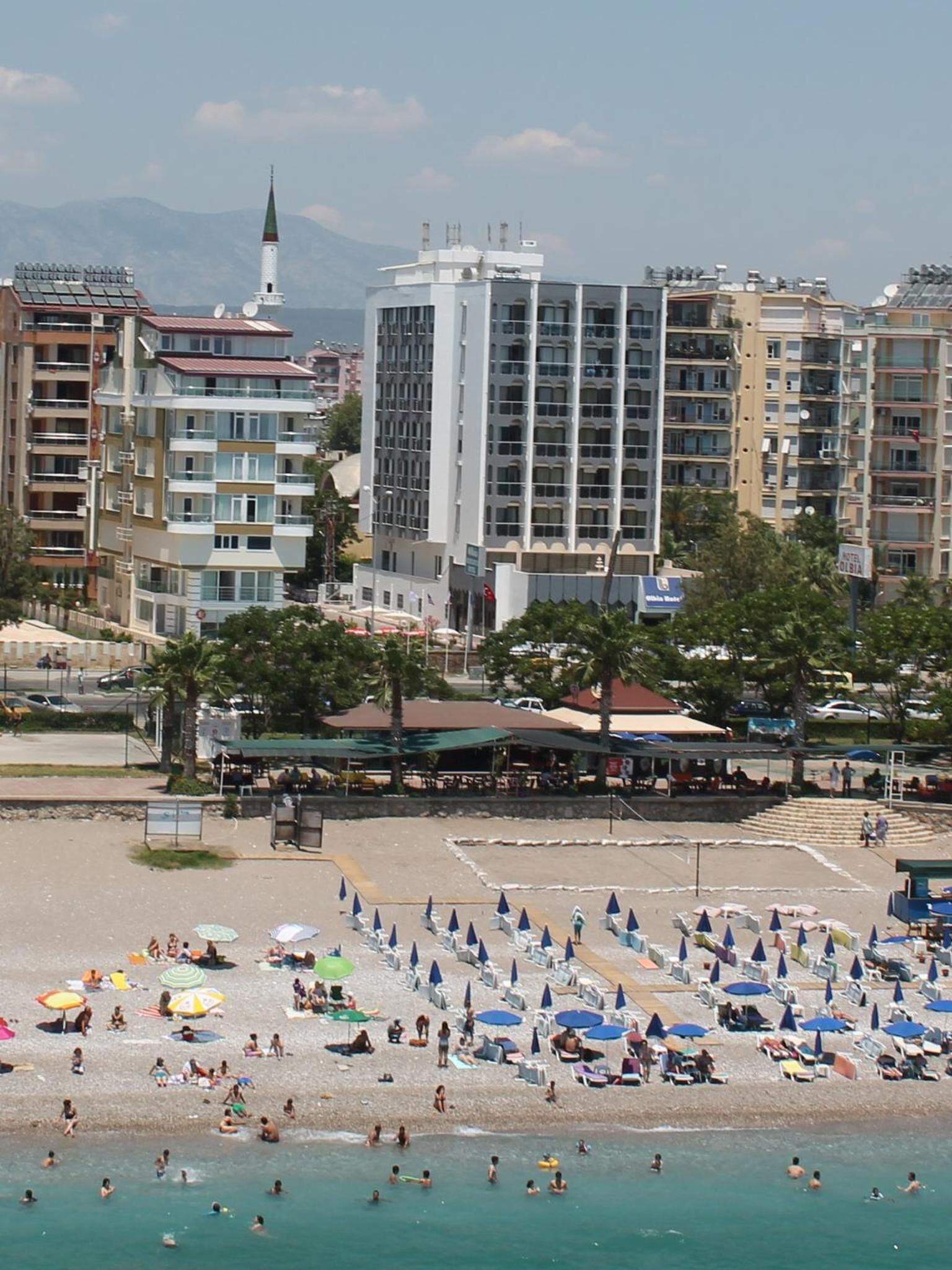 Una playa con sombrillas y gente. Se ven edificios al fondo.