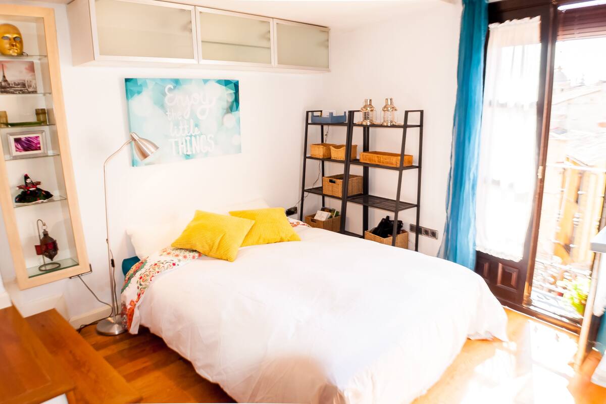 A bedroom with a bed, a bookshelf, a desk, and a window with curtains.