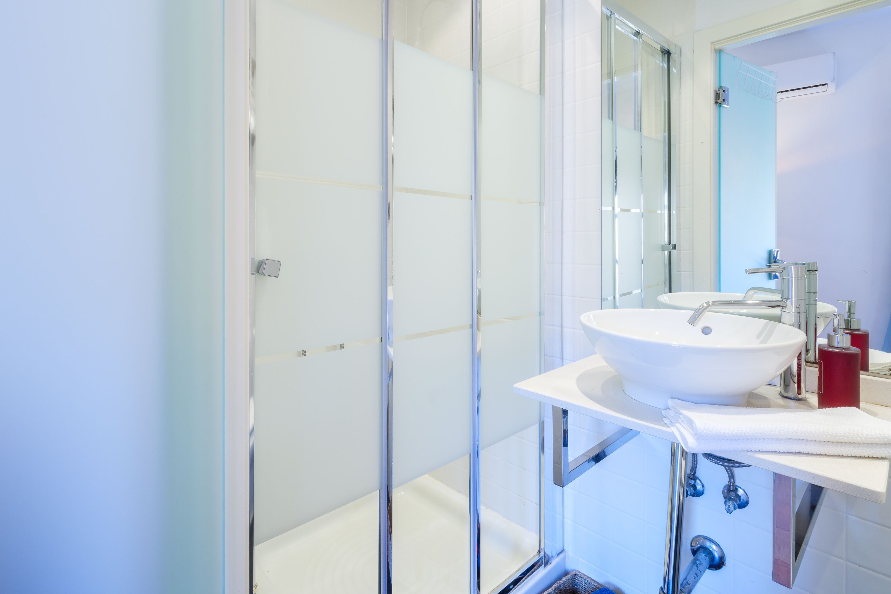 A modern bathroom with a glass shower enclosure, a white sink, and a mirror above the sink.