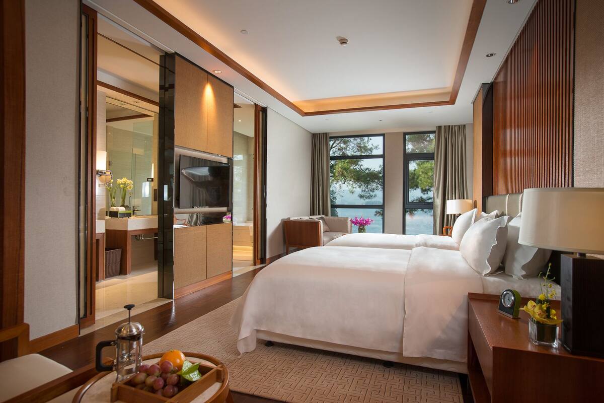 Quarto de hotel com uma cama grande, televisão, secretária com abajur e vista para o exterior.