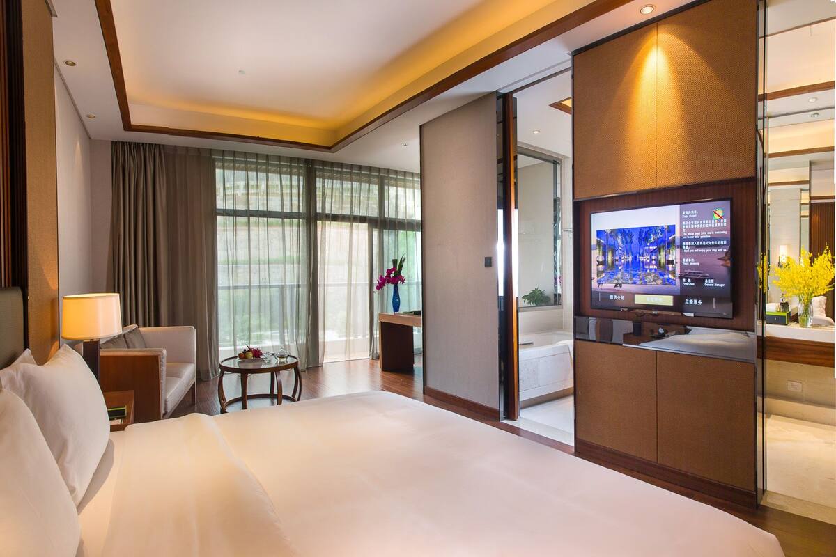 Quarto de hotel com cama, escrivaninha, televisão e vista para o exterior.