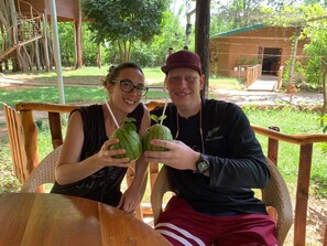 Two people sitting at a wooden table outdoors, holding watermelons. - La Pentera (Thanamalvila)