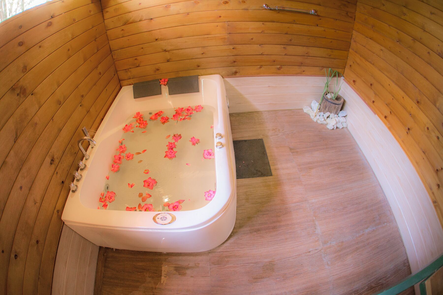 Une cabane en bois avec une baignoire remplie d’eau et de pétales de rose.