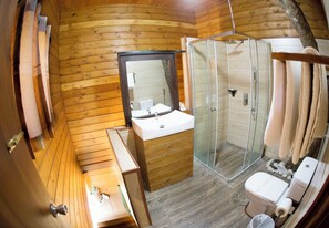 A wooden cabin bathroom with a wooden vanity, a sink, a mirror, a glass shower enclosure, and a toilet. - La Pentera (Thanamalvila)