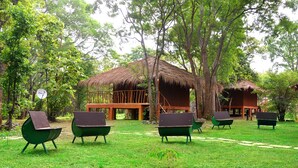 A thatched-roof structure with a wooden deck, surrounded by lush greenery and outdoor seating. - La Pentera (Thanamalvila)