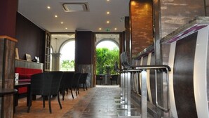 A hotel lobby with a long reception desk, black chairs, and a staircase with metal railings.