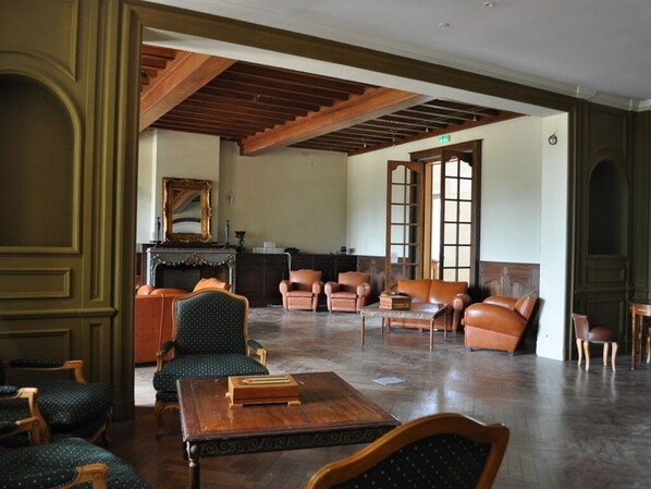 A spacious room with wooden flooring, a large wooden table, and several leather armchairs.