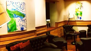 A lounge area with a sofa, armchairs, and a coffee table. There are paintings on the walls and a lamp on a table. - arthausHOTEL (Davos)