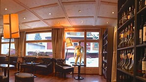 A spacious living area with a wooden floor, a sofa, a coffee table, and a lamp. There is a large window with a view of a snowy landscape. - arthausHOTEL (Davos)