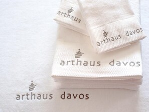 A stack of white towels with embroidered text "arthaus davos". - arthausHOTEL (Davos)