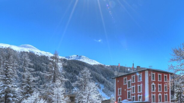 A red building with multiple windows, surrounded by snow-covered trees and mountains in the background. - arthausHOTEL (Davos)