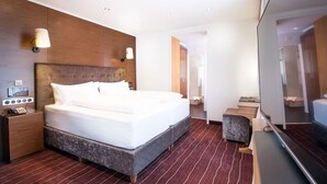 A modern hotel room with a large bed, a wooden headboard, a nightstand with a phone, and a mirror. - arthausHOTEL (Davos)