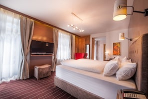 A modern hotel room with a large bed, a flat-screen TV, a wooden headboard, and a red accent wall. - arthausHOTEL (Davos)