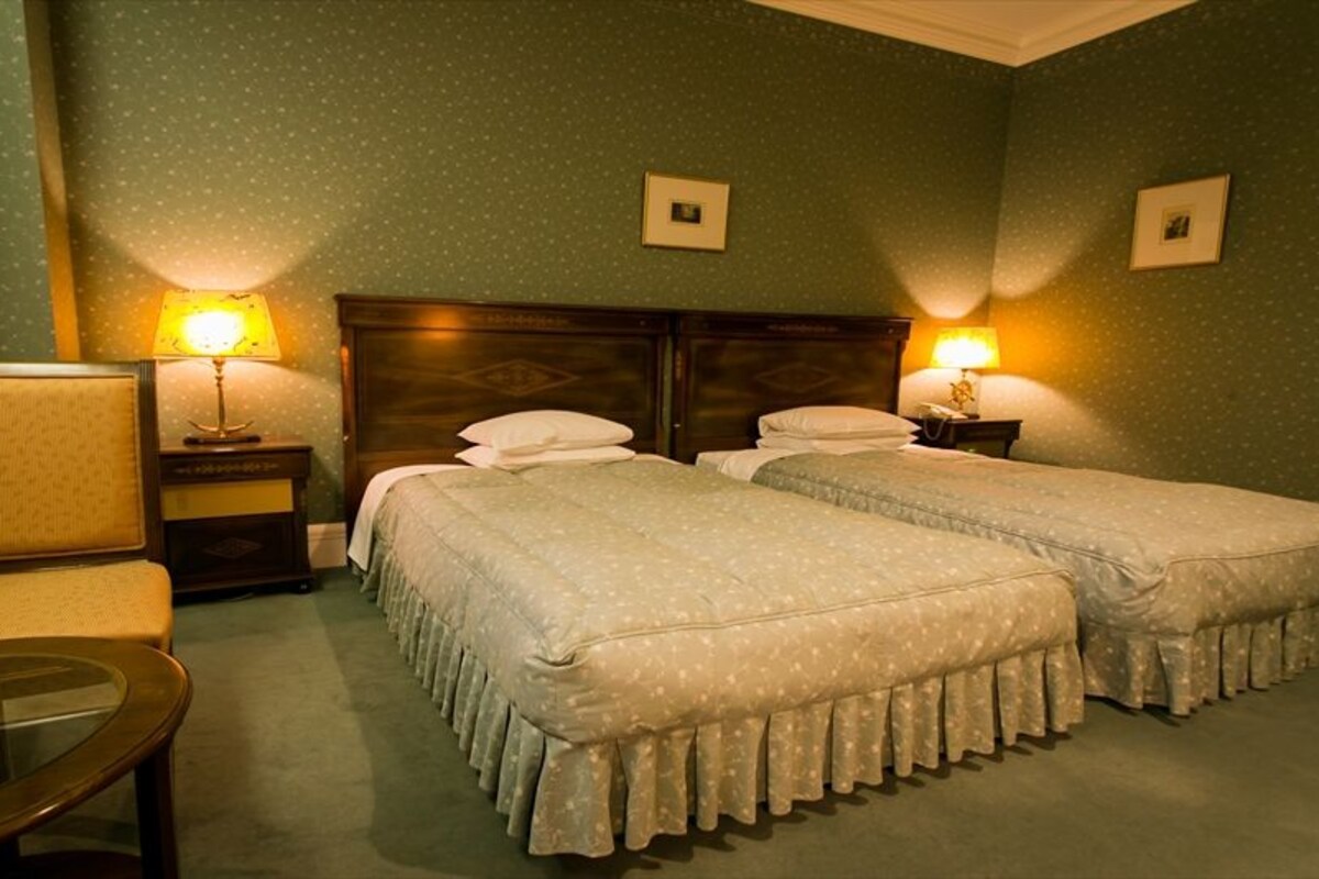 Ein Hotelzimmer mit zwei Betten, einem Sessel, einem kleinen Tisch und zwei Nachttischlampen.