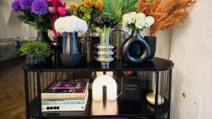 A black console table with a variety of decorative items including books, a small lamp, and floral arrangements. - Hotel Maxplatz (Hof)