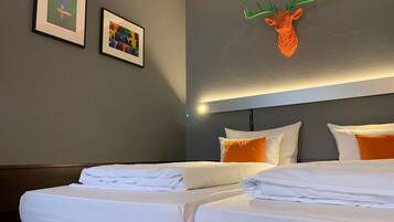 A hotel room with two beds, white bedding, a headboard with orange accents, and two framed artworks on the wall.