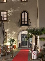 Una entrada con alfombra roja, una palmera y un edificio con ventanas de arco.