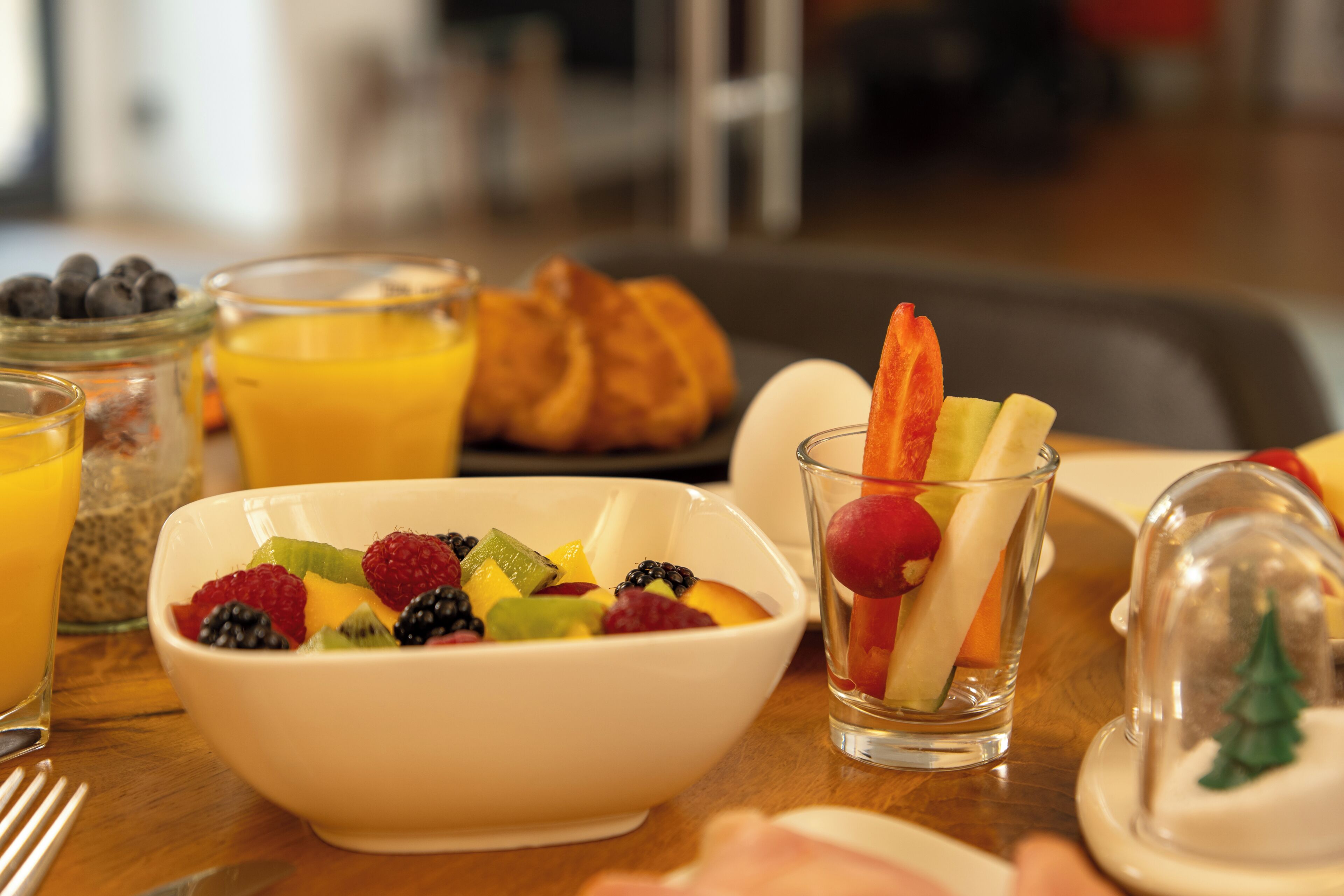 Ein Frühstückstisch mit einer Schüssel Obstsalat, einem Glas Orangensaft und einem Glas Wasser.