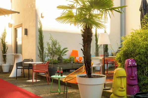 An outdoor seating area with tables and chairs, surrounded by potted plants and a statue.