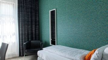 A hotel room with a bed, a chair, a window with curtains, and a textured green wall.